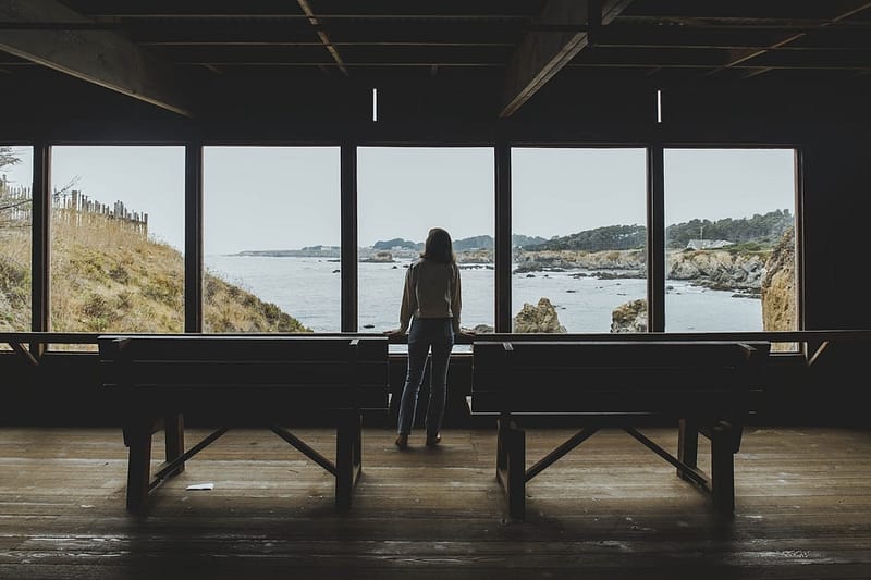 a woman looking at the ocean from inside a wooden building