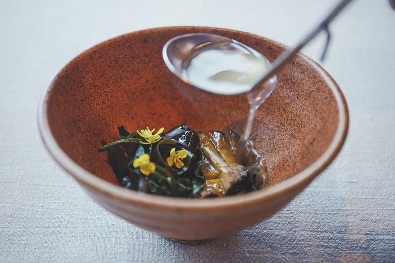 a ladle pouring broth into a bowl of seaweed