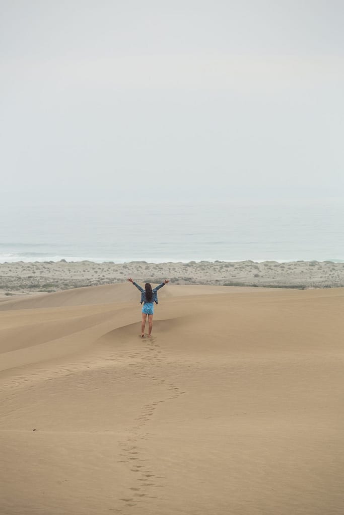 a woman in the dunes raising her arms towards the ocean