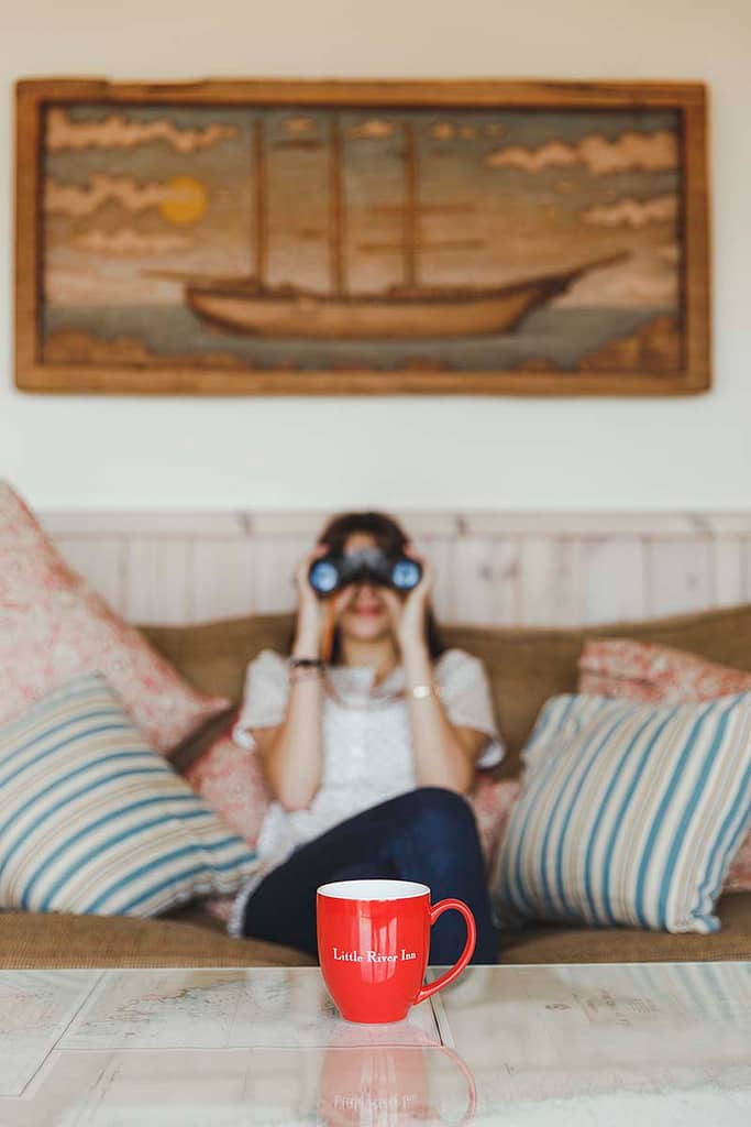 Woman looking through binoculars with coffee mug