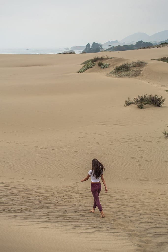 a woman walking across sand dunes