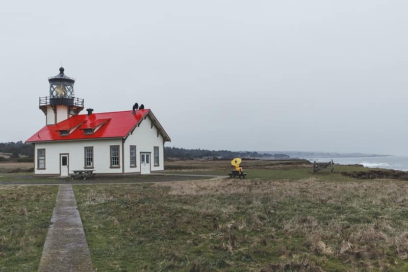 a woman sitting on a picnic table in front of the lighthouse