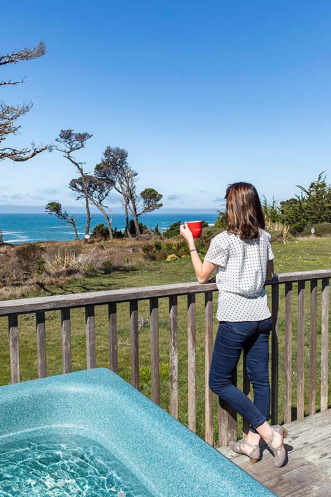Woman standing next to hot tub looking over ocean near Mendocino in hotel room