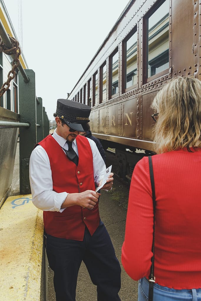 a conductor in a red vest punching a ticket